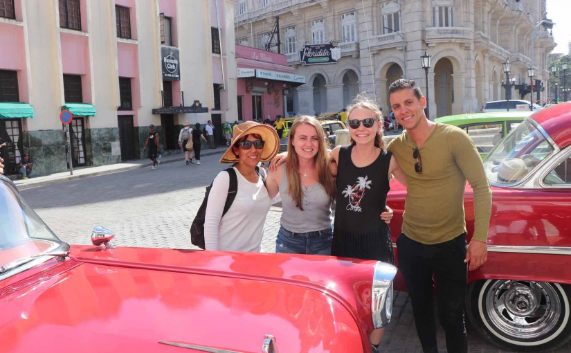 family in front of red classic car in Havana