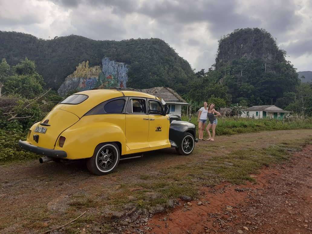 yellow and black classic car in viñales mountains in cuba with girls far away